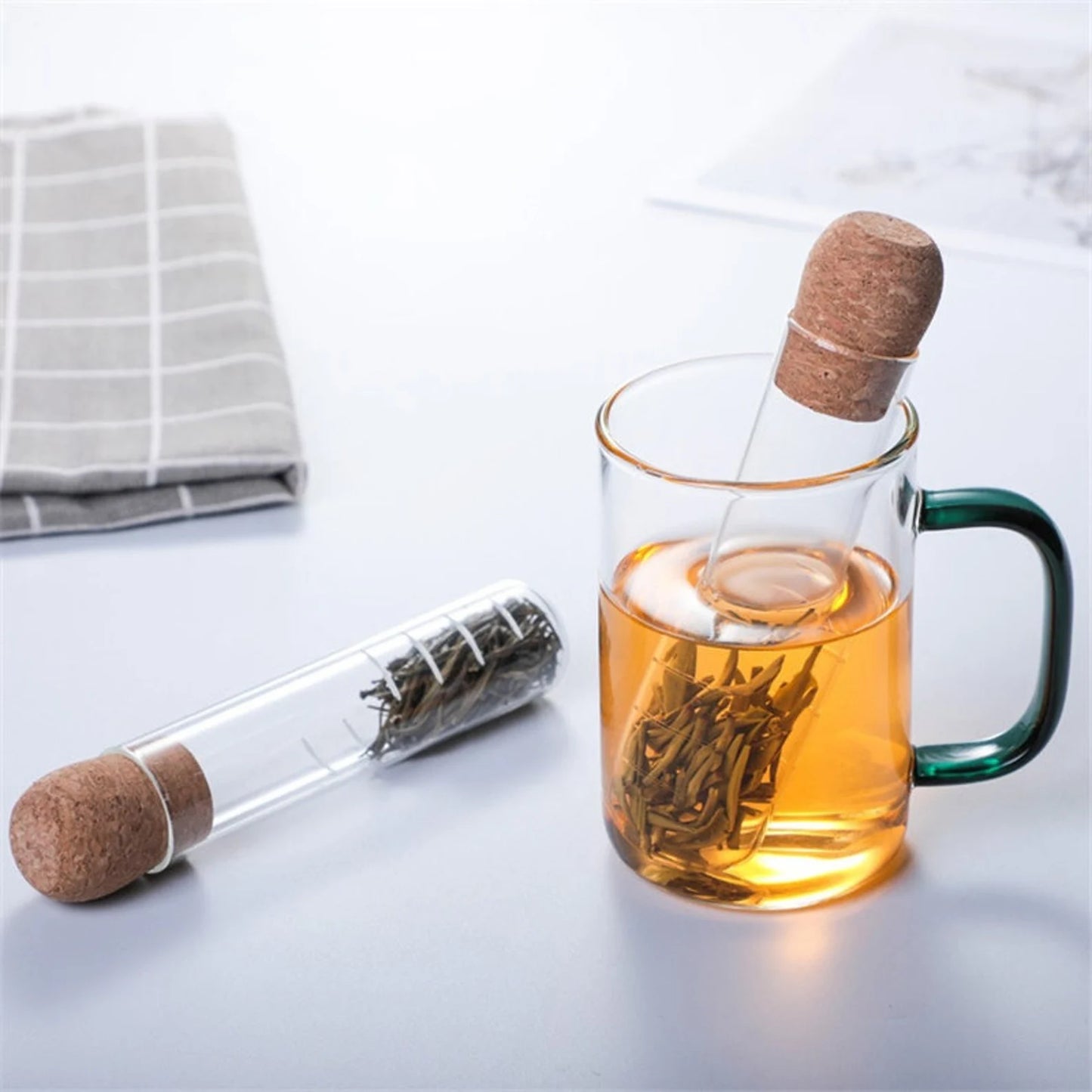 A tea infuser used for brewing loose leaf herbal tea sitting in a glass tea cup on a table next to another tea infuser with herbal tea inside next to a napkin.